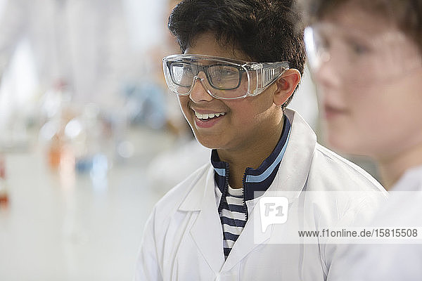 Lächelnder Junge mit Schutzbrille und Laborkittel in einem Laborklassenzimmer