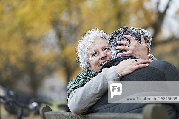 Lächelndes  zärtliches älteres Paar  das sich auf einer Bank im Herbstpark umarmt