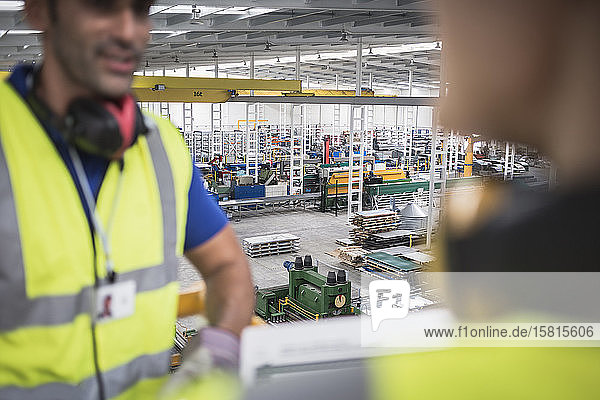 Männliche Arbeiter unterhalten sich auf einer Plattform in einer Fabrik