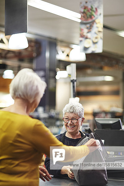 Friendly senior female cashier helping customer supermarket checkout