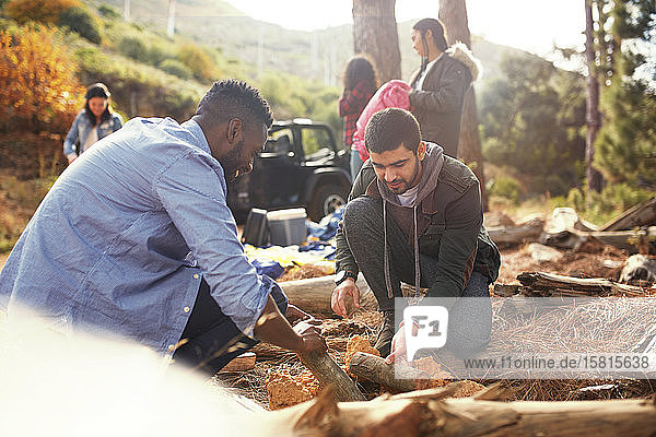 Junge Männer und Freunde bauen ein Lagerfeuer auf einem Campingplatz