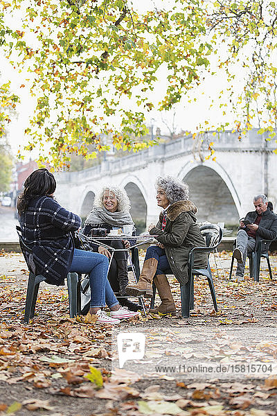 Lächelnde  aktive Seniorinnen  die im Herbst im Parkcafé Kaffee trinken