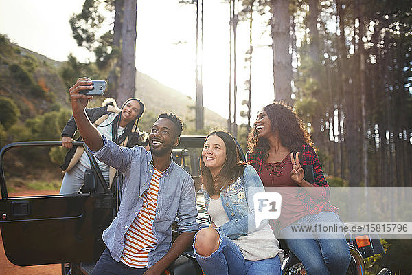 Junge Freunde mit Fotohandy machen ein Selfie von einem Jeep im Wald