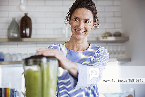 Smiling woman making healthy green smoothie in kitchen