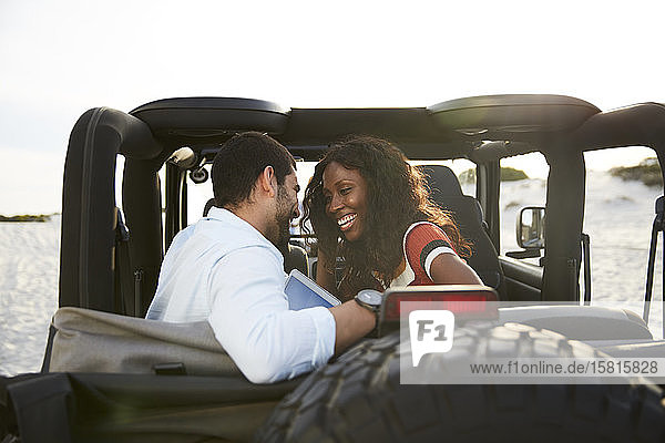 Zärtliches junges Paar lächelt auf dem Rücksitz eines Jeeps und genießt die Autofahrt
