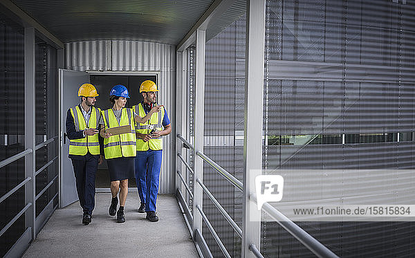 Supervisors with clipboard walking and talking on elevated walkway outside factory