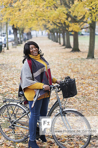 Portrait smiling  confident woman bike riding among trees and leaves in autumn park