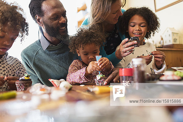 Multiethnische Familie beim Verzieren von Cupcakes am Tisch