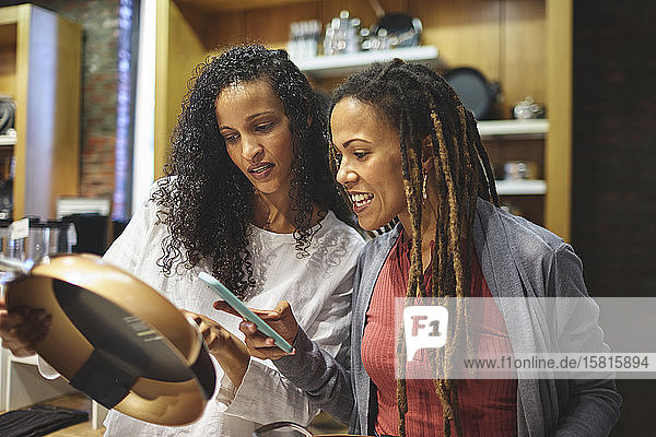 Freundinnen mit Smartphone beim Einkaufen einer Bratpfanne