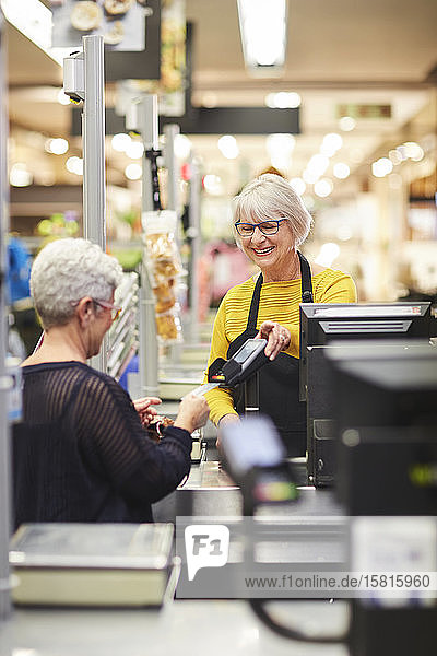 Senior female cashier helping customer at supermarket checkout
