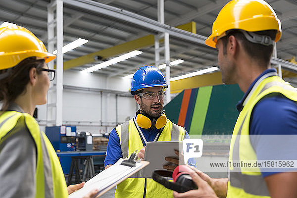 Vorgesetzter und Arbeiter mit Klemmbrett und digitalem Tablet im Gespräch in einer Fabrik