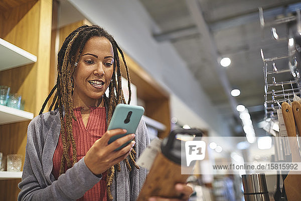 Frau mit Smartphone beim Einkaufen in einem Haushaltswarengeschäft