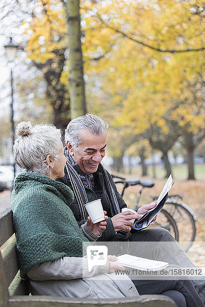 Älteres Paar liest Zeitung und trinkt Kaffee auf einer Bank im Herbstpark