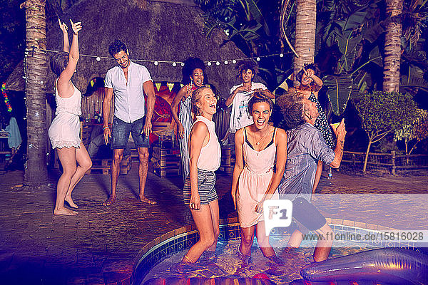 Begeisterte junge Freunde tanzen und hängen bei einer nächtlichen Sommerparty am Pool herum