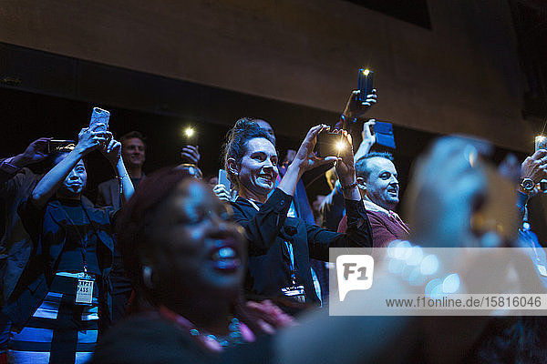 Smiling  enthusiastic audience using camera phones in dark auditorium