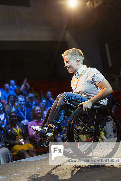 Smiling female speaker doing a wheelie in wheelchair on stage