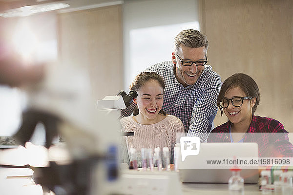 Male teacher and girl students conducting scientific experiment at microscope and laptop in laboratory classroom
