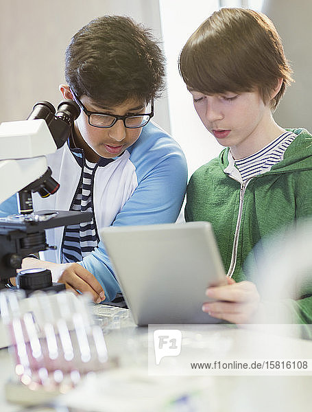 Junge Schüler  die ein digitales Tablet und ein Mikroskop benutzen und ein wissenschaftliches Experiment im Labor durchführen