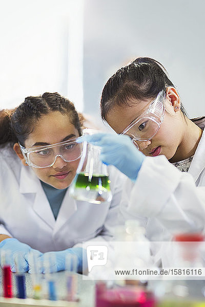 Girl students examining liquid in beaker conducting scientific experiment in laboratory classroom