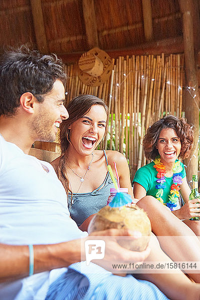 Lachende junge Freunde  die am Sommerpool einen Kokosnusscocktail trinken