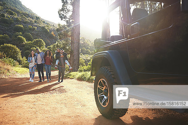 Junge Freunde gehen auf einem sonnigen Feldweg im Wald auf einen Jeep zu