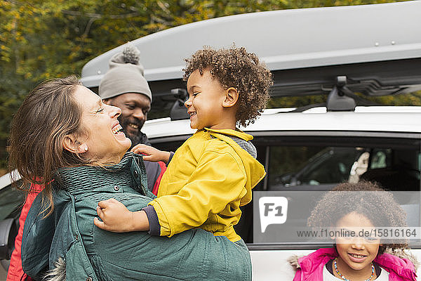 Happy family hugging outside car in parking lot