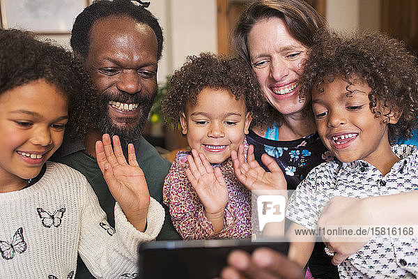 Glückliche multiethnische Familie winkt und chattet mit dem Smartphone