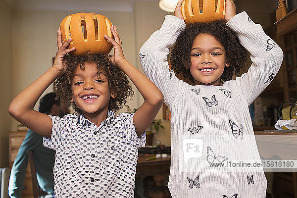 Portrait of happy brother and sister holding carved pumpkins overhead