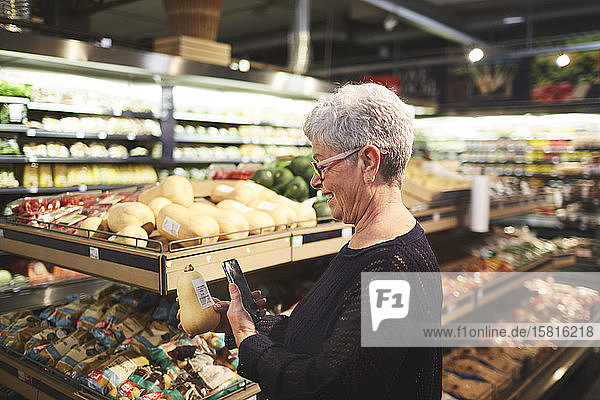 Ältere Frau mit Smartphone beim Einkaufen in der Lebensmittelabteilung eines Supermarkts