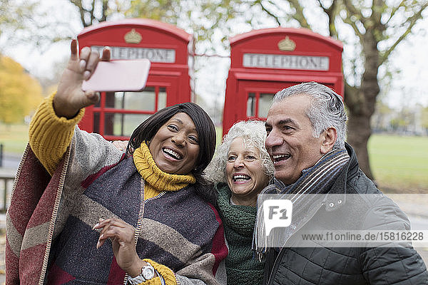 Ältere Freunde machen ein Selfie vor einer roten Telefonzelle im Herbstpark