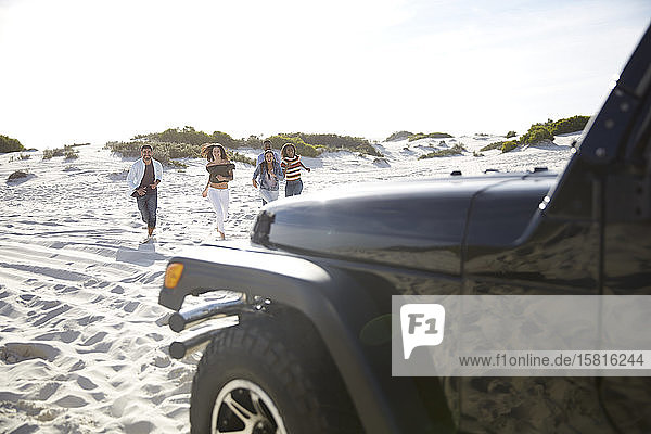 Junge Freunde laufen am sonnigen Strand in Richtung Jeep