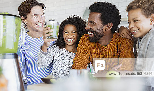 Smiling multi-ethnic family drinking healthy green smoothie in kitchen