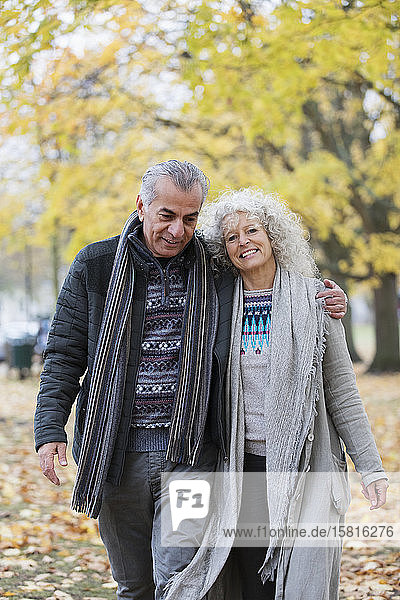 Selbstbewusstes  lächelndes älteres Paar  das sich umarmt und im Herbstpark spazieren geht