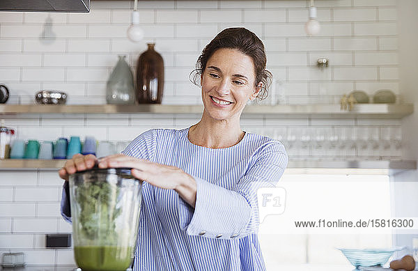 Lächelnde Frau bei der Zubereitung eines gesunden grünen Smoothies in einem Mixer in der Küche