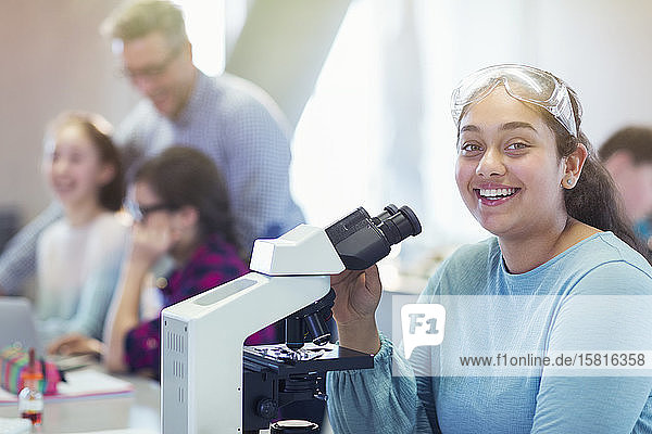 Porträt einer lächelnden  selbstbewussten Studentin  die ein wissenschaftliches Experiment am Mikroskop in einem Laborklassenzimmer durchführt