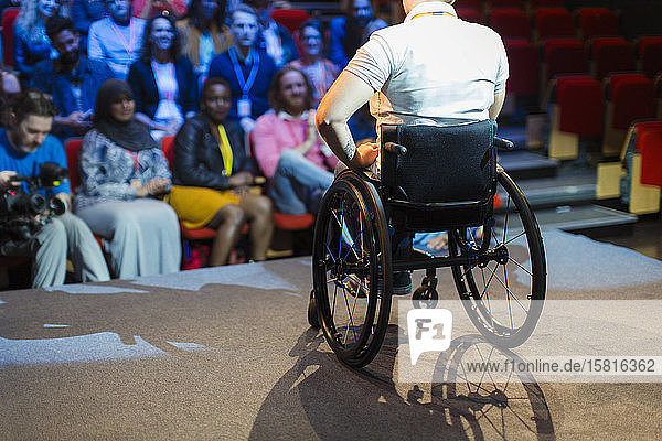 Publikum beobachtet Rednerin im Rollstuhl auf der Bühne