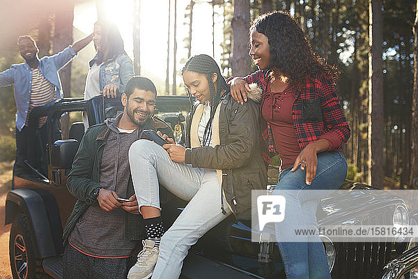 Junge Freunde  die auf einem Jeep mit ihrem Smartphone SMS schreiben und einen Roadtrip genießen