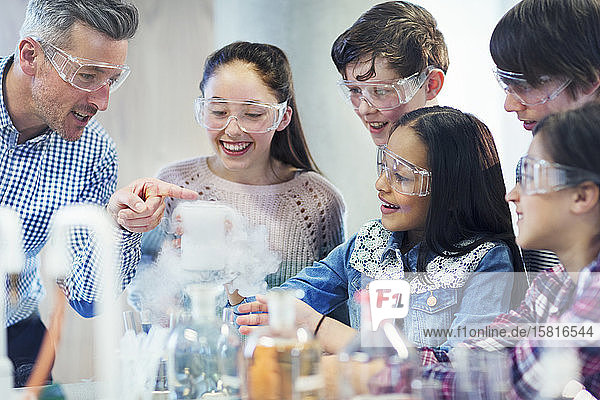 Male teacher and students watching chemical reaction  conducting scientific experiment in laboratory classroom