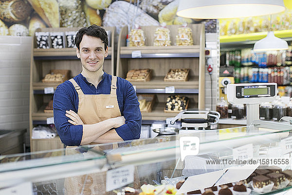 Portrait confident male worker behind bakery display case in supermarket