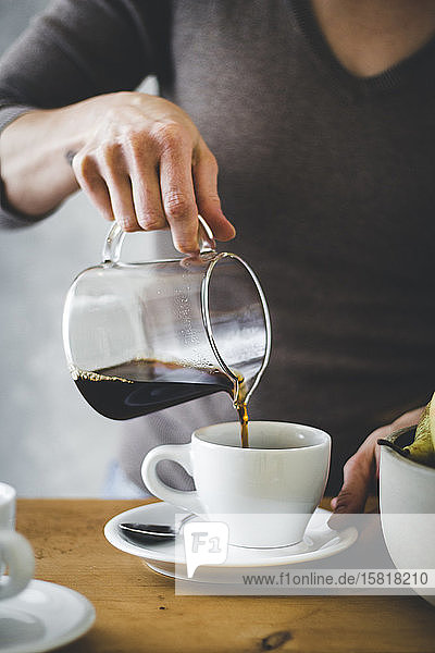 Frauenhand gießt Kaffee in eine Kaffeetasse