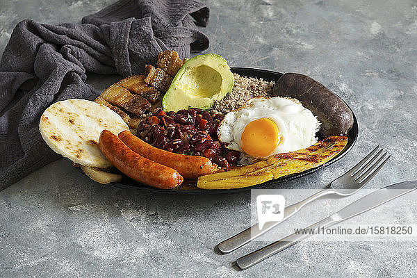 Bandeja paisa - kolumbianischer gebratener Schweinebauch  Blutwurst  Wurst  Arepa  Bohnen  gebratene Kochbananen  Avocado-Ei und Reis