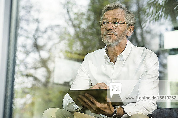Älterer Mann mit grauen Haaren in modernem Design-Wohnzimmer mit auf der Couch sitzendem Tablett