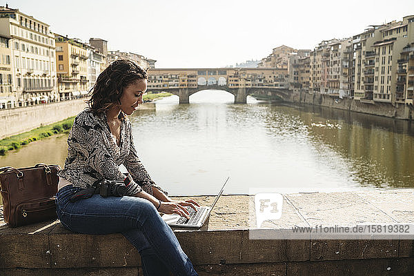 Young woman using laptop on a bridge  Florence  Italy