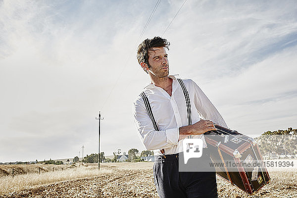 Man in old-fashioned clothes with suitcase in the countryside