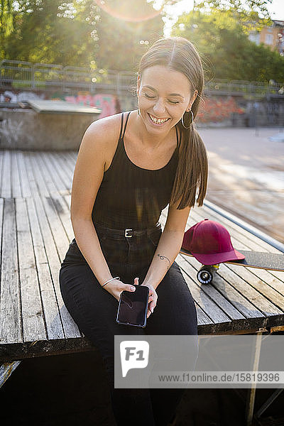 Junge lachende Frau mit Smartphone im Skatepark