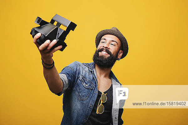 Bearded young man in studio taking selfie with instant camera