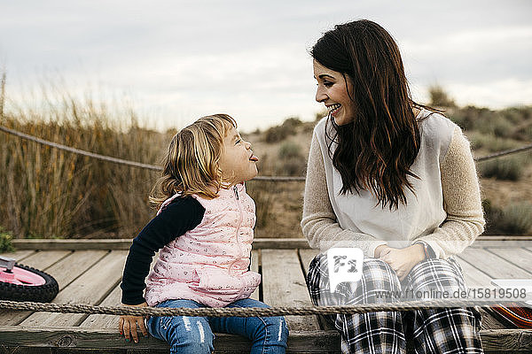 Happy mother and cheeky daughter sitting on a boardwalk in the countryside