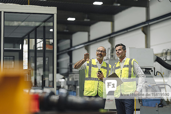 Zwei Männer in reflektierenden Westen sprechen in einer Fabrik