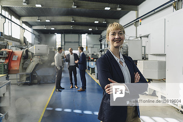 Portrait of a confident businesswoman in a factory with colleagues in backgound