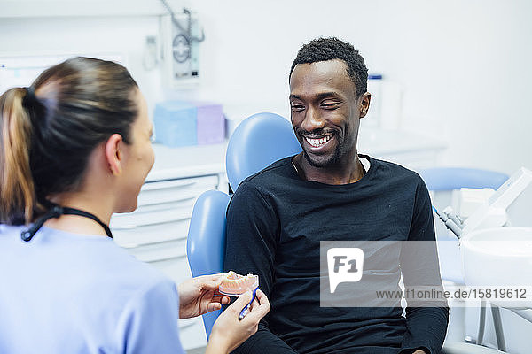 Zahnärztin zeigt lächelnden Patienten Zahnersatz in der medizinischen Praxis